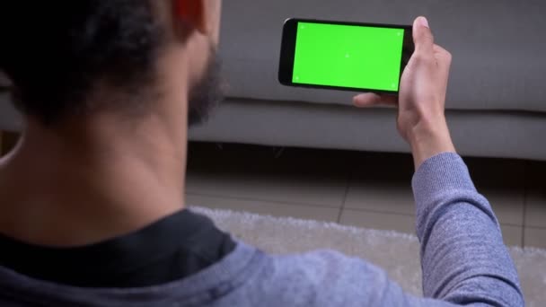 Gros plan vue de dos pousse de la main masculine afro-américaine tenant un téléphone avec écran vert à l'intérieur dans l'appartement — Video