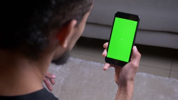 Närbild tillbaka se skjuta av afrikansk amerikansk manlig bloggare streaming live hålla en telefon med grön Chroma skärm inomhus i lägenhet — Stockvideo