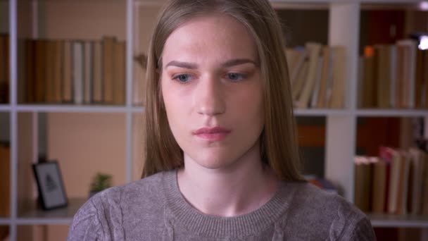 Gros plan portrait de jeune étudiante attrayante aux cheveux longs regardant la caméra dans la bibliothèque du collège à l'intérieur — Video