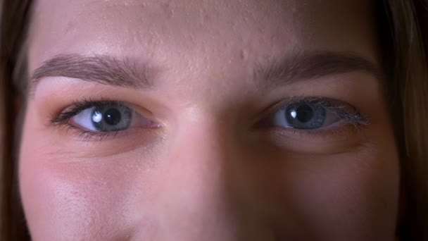 Nahaufnahme eines jungen brünetten weiblichen Gesichts mit Augen, die mit lächelndem Gesichtsausdruck in die Kamera schauen — Stockvideo