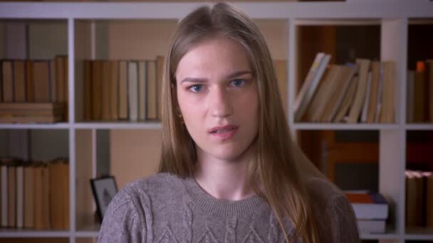 Retrato de cerca de una joven estudiante atractiva agitando la cabeza diciendo no con ira mirando a la cámara en la biblioteca de la universidad en el interior — Vídeos de Stock