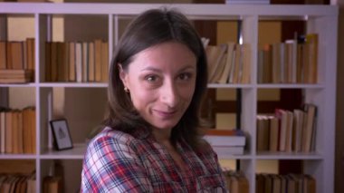 Kütüphanede kapalı kameraya bakarak güvenle gülümseyen genç çekici kız öğrencinin closeup çekimi