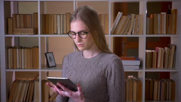 태블릿을 사용하여 안경에 젊은 매력적인 여학생의 클로즈업 초상화와 실내 대학 도서관에서 카메라에 녹색 화면을 보여주는 — 비디오