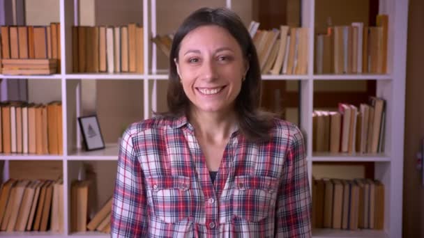 Nahaufnahme einer jungen attraktiven Studentin, die glücklich in die Kamera in der Bibliothek lächelt — Stockvideo