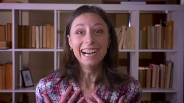 Nahaufnahme einer jungen attraktiven Studentin, die aufgeregt und überrascht in die Kamera in der Universitätsbibliothek blickt — Stockvideo