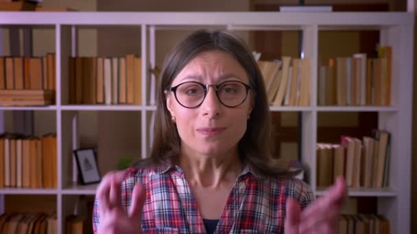 Closeup shoot of young attractive female student having her fingers crossed being anxious looking at camera in the library indoors — Stock Video