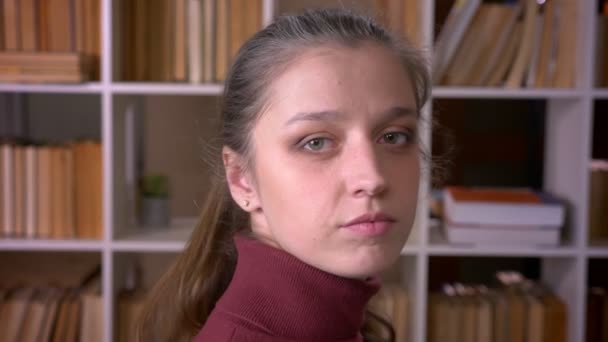 Närbild porträtt av unga kaukasiska kvinnliga studenten vrida och titta på kamera i kollegiet biblioteket inomhus — Stockvideo