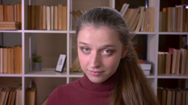 Närbild porträtt av unga kaukasiska kvinnlig student leende glatt tittar på kameran i kollegiet biblioteket inomhus — Stockvideo