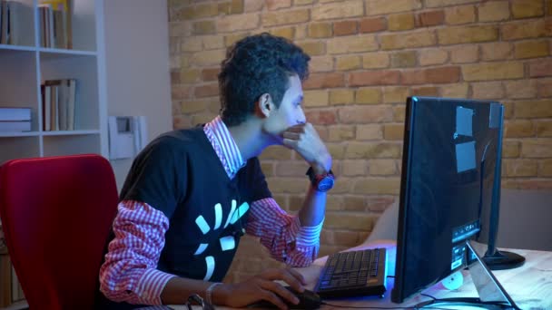 Крупним планом знімок молодого індійського привабливого чоловіка, який друкує на ноутбуці, сидячи в приміщенні в затишній квартирі з неоновим світлом — стокове відео
