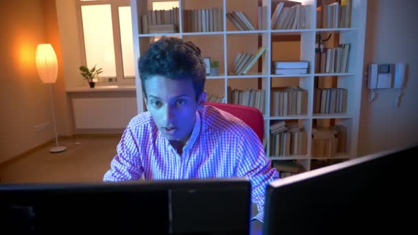 Primer plano de brote de joven indio atractivo macho jugando videojuegos en el ordenador sentado en el interior en el acogedor apartamento con luz de neón — Vídeos de Stock