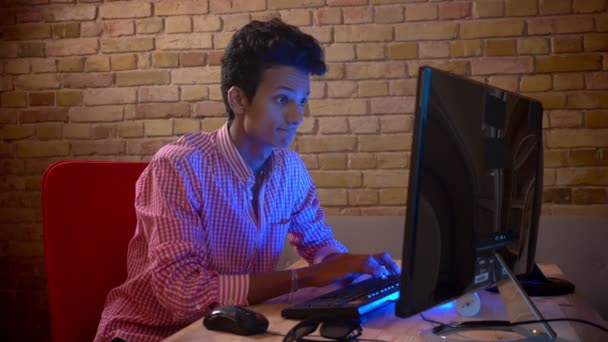 Съемки крупным планом молодого индийца, привлекательного мужчины, играющего в видеоигры на компьютере, в уютной квартире с неоновым светом — стоковое видео
