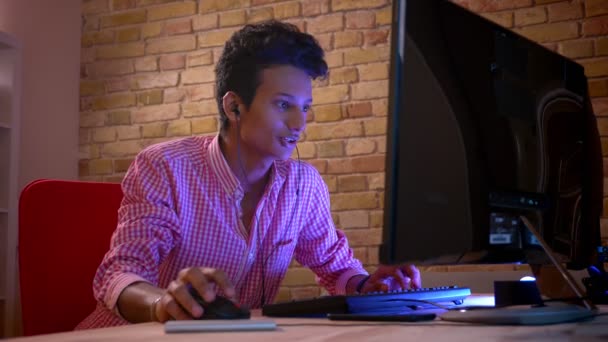 Sesión de primer plano de joven blogger masculino atractivo indio en vibraciones jugando videojuegos en el ordenador interior en el acogedor apartamento con luz de neón — Vídeo de stock