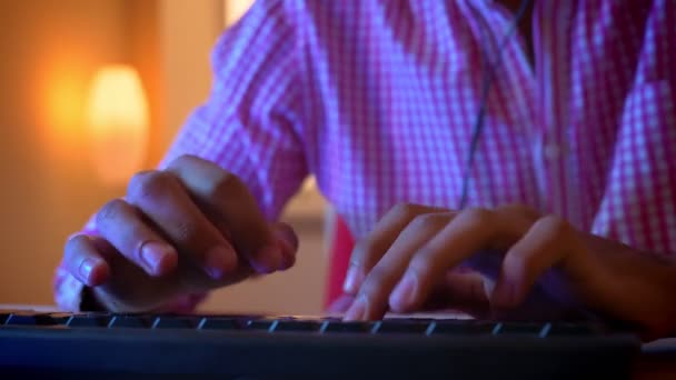 Κοντινά πλάνα του Ινδικού αρσενικό blogger χέρια δακτυλογραφούν στο πληκτρολόγιο σε εσωτερικούς χώρους σε ένα άνετο διαμέρισμα με νέον φως — Αρχείο Βίντεο