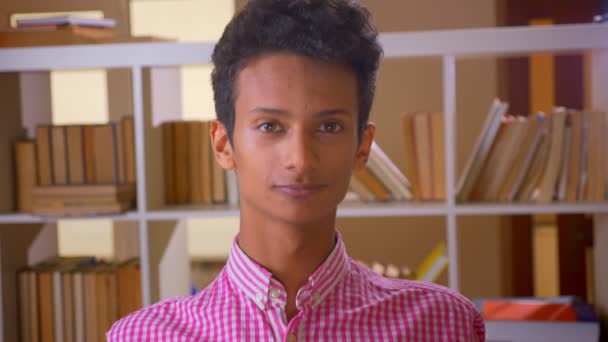 Närbild shoot of Young lockar indiska manliga nickande och tittar på kameran i kollegiet biblioteket inomhus — Stockvideo