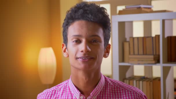 Genç attractice hint erkek kapalı üniversite kütüphanesinde kameraya mutlu bakarak gülümseyen Closeup ateş — Stok video