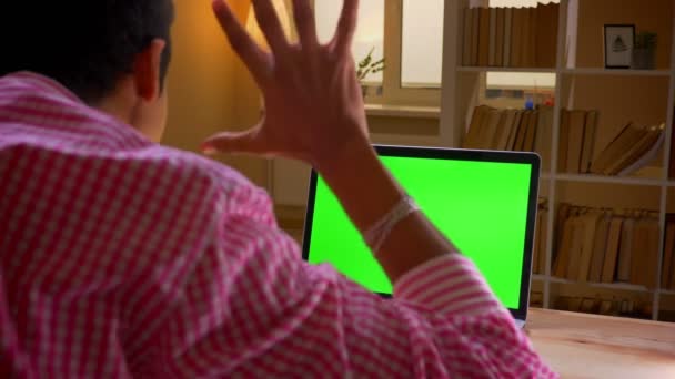 Primo piano vista posteriore ripresa di indiano giovane uomo d'affari avendo una videochiamata sul computer portatile con schermo verde in ufficio al chiuso — Video Stock
