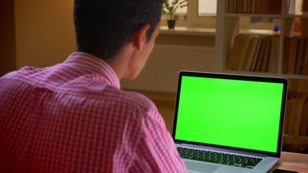 실내 사무실에서 녹색 크로마 스크린이있는 노트북에서 화상 통화를하는 인도의 젊은 사업가의 클로즈업 백뷰 촬영 — 비디오