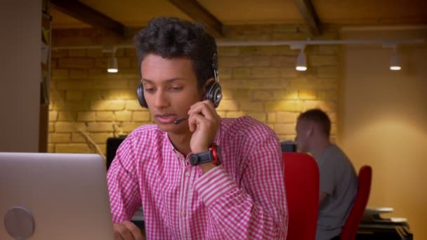 Kapalı ofiste dizüstü bilgisayar kullanarak kulaklık Hintli genç işadamıcloseup çekim — Stok video