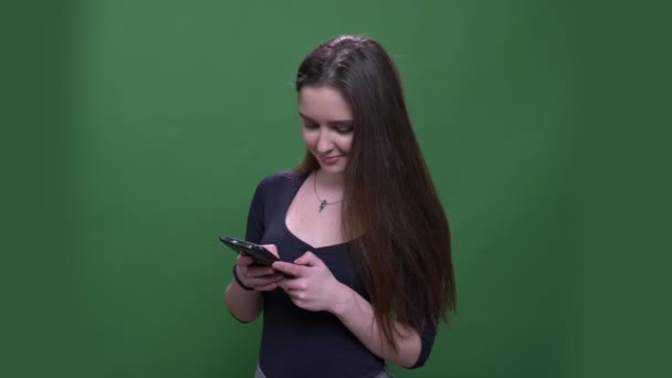 Primer plano retrato de joven guapa morena hembra usando el teléfono y sonriendo felizmente con fondo aislado en verde — Vídeos de Stock