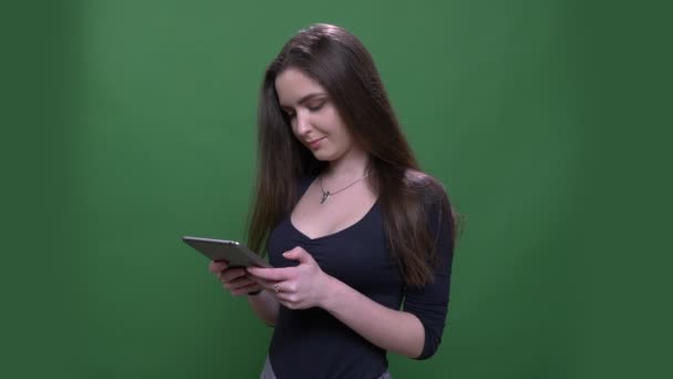 Close-up portret van jonge mooie brunette vrouw met behulp van de Tablet en glimlachend gelukkig met achtergrond geïsoleerd op groen — Stockvideo