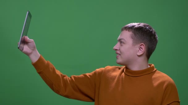 Střílejí mladého přitažlivého bělošského muže, který má video hovor na tabletu s pozadím izolovaným na zeleném — Stock video
