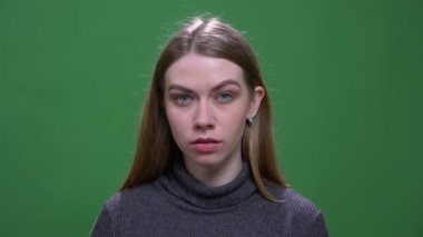 Sakince ve dikkatle izleyen genç sarışın model yeşil renkli arka planda izole edilmiş kameraya bakıyor..