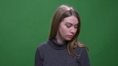 Genç sarışın manken, yeşil renkli arka planda düşünceli bir şekilde izole edilişini izliyor..
