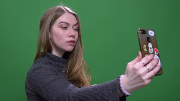 Beautiful blonde businesswoman making selfies using smartphone isolated on green chromakey background.