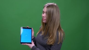 Genç sarışın iş kadını yeşil renkli arka planda izole edilmiş mavi renkli tablet gösteriyor..