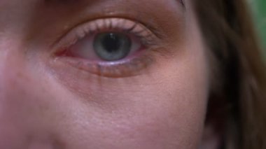 Sarışın modelin yakın çekim bir göz portresi yeşil renk arka planda kameraya sakin ve dikkatle saatler.