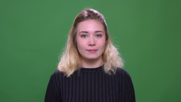 Closeup portré fiatal csinos szőke kaukázusi nő integetett Szia mosolyogva nézi kamera háttérrel izolált zöld — Stock videók