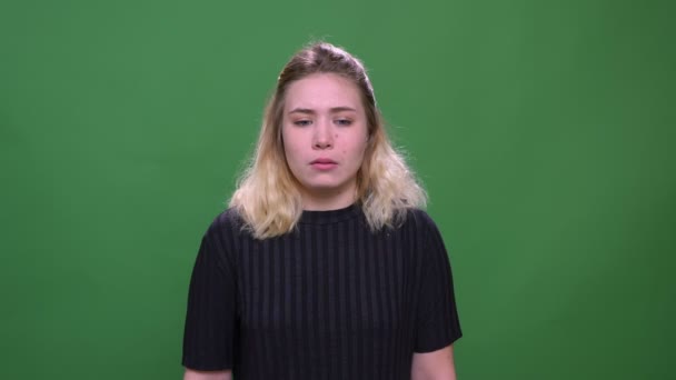 Nahaufnahme Porträt einer jungen hübschen blonden kaukasischen Frau, die verwirrt und nachdenklich in die Kamera schaut, mit Hintergrund isoliert auf grün — Stockvideo