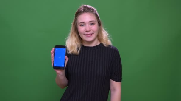 Close-up retrato de jovem bonita loira caucasiano feminino usando o telefone e mostrando tela azul para câmera com fundo isolado no verde — Vídeo de Stock