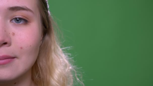 Primo piano mezzo volto sparare di giovane attraente viso femminile caucasico con gli occhi guardando la fotocamera con sfondo isolato su verde — Video Stock