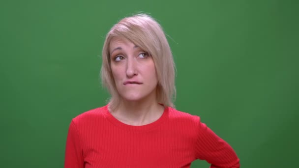 Блондинка середнього віку короткошерста модель задумливо кусає губи ізольовано на зеленому фоні . — стокове відео