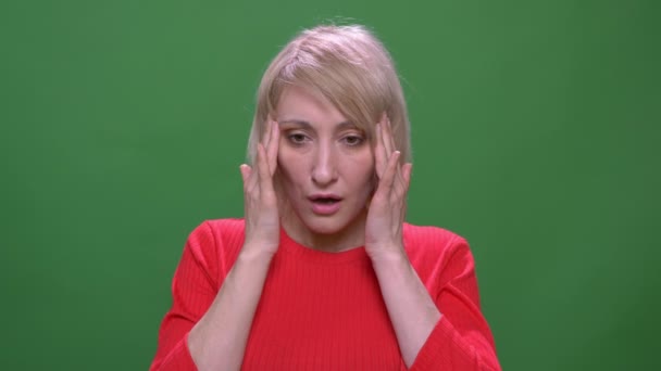 Middle-aged blonde short-haired model suffers from migraine isolated on green background. — Stock Video