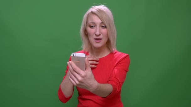 Middle-aged short-haired businesswoman talks in videochat on smartphone isolated on green chromakey background.
