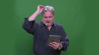 Kıdemli gri saçlı işadamı yeşil renk arka plan izole tablet ile çalışan gözlük çıkarır.