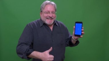 Kıdemli işadamı yeşil renk arka plan üzerinde izole uygulaması ile telefonun mavi ekranda thumb-up gösterir.