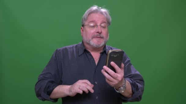 Üst düzey gri saçlı Amerikalı adam telefonda videochat konuşurken yeşil renk arka plan izole. — Stok video