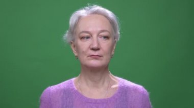 Mor kazak kıdemli gri saçlı kadın yeşil renk arka plan izole kamera içine sakince saatler.
