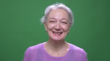 Mor kazak kıdemli gri saçlı kadın yeşil renk arka plan izole kamera içine güzel gülümsüyor.