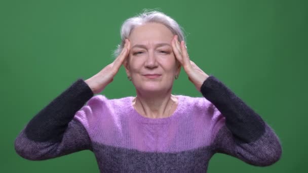 Retrato de mulher de cabelos grisalhos sênior sofre de dor de garganta e dor de cabeça isolada em fundo cromado verde . — Vídeo de Stock