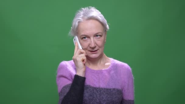 Senior donna dai capelli grigi in maglione viola parla sul cellulare isolato su sfondo cromakey verde . — Video Stock