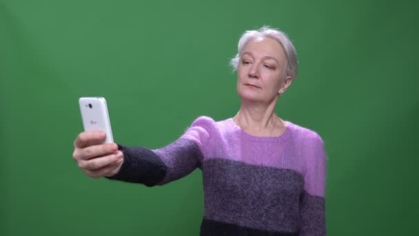 Senior grauhaarige Frau in violettem Pullover macht Selfies auf Smartphone isoliert auf grünem Chromakey-Hintergrund. — Stockvideo