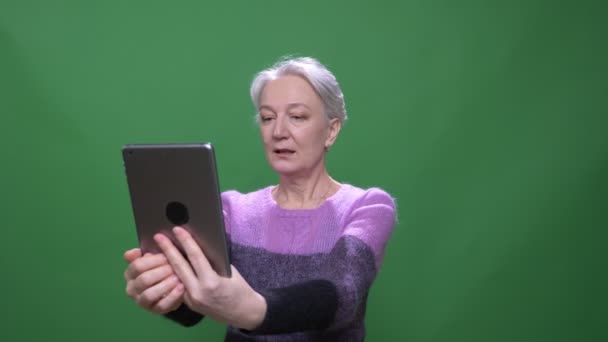 Senior donna dai capelli grigi in viola maglione parla in videochat su tablet isolato su sfondo cromakey verde . — Video Stock