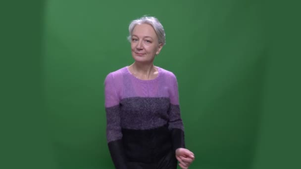 Старша сіро-волохата жінка в фіолетовому светрі танцює скромно ізольовано на зеленому хромосовому фоні . — стокове відео