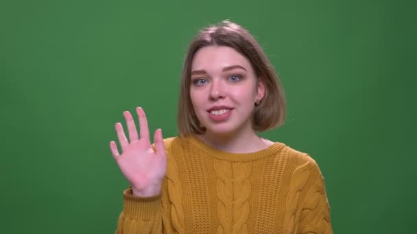 Närbild shoot av unga attraktiva korthårig kvinnlig viftande Hej leende glatt tittar på kamera med bakgrund isolerade på grön — Stockvideo