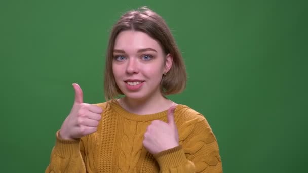 Gros plan tige de jeune jolie femelle aux cheveux courts montrant un pouce vers le haut souriant regardant caméra avec fond isolé sur vert — Video