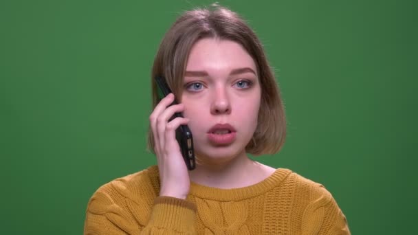 Съемки крупным планом молодой привлекательной коротковолосой женщины с телефонным звонком, смотрящей в камеру с изолированным фоном на зеленом — стоковое видео